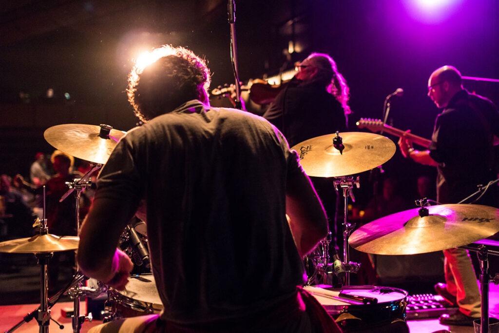 Man playing a drum set in a band on stage.