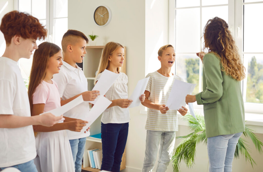 Young school children standing in a circle with their young female teacher having singing lessons