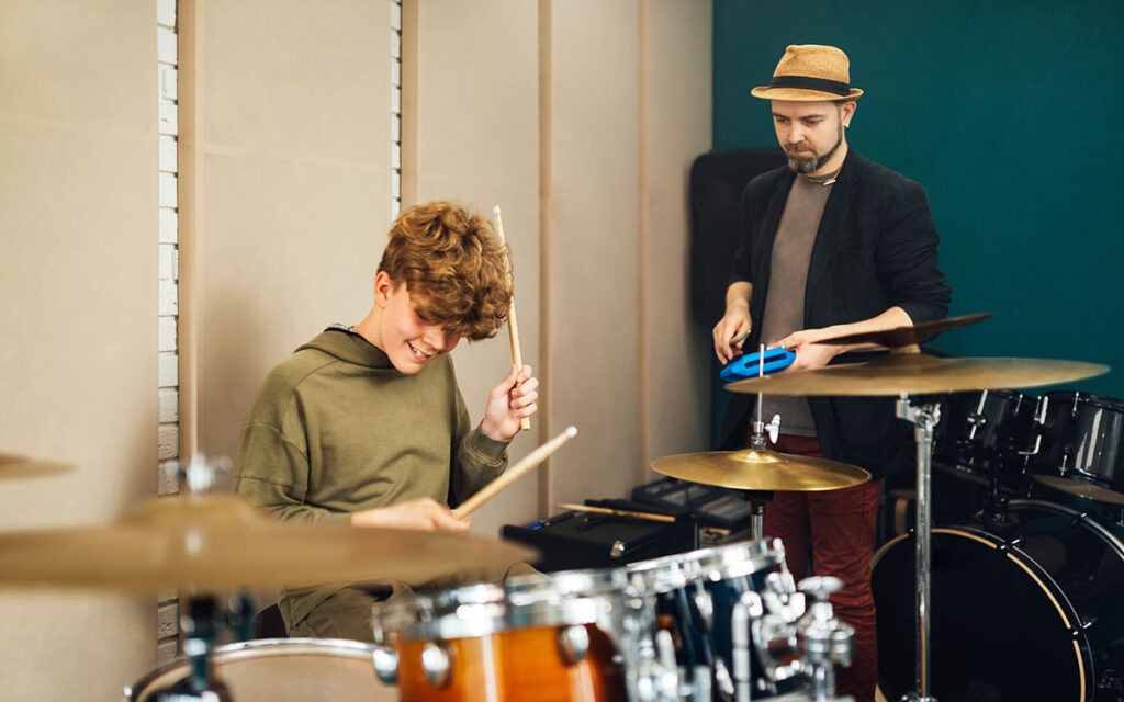 Male drum instructor teaching young male student on a drum set