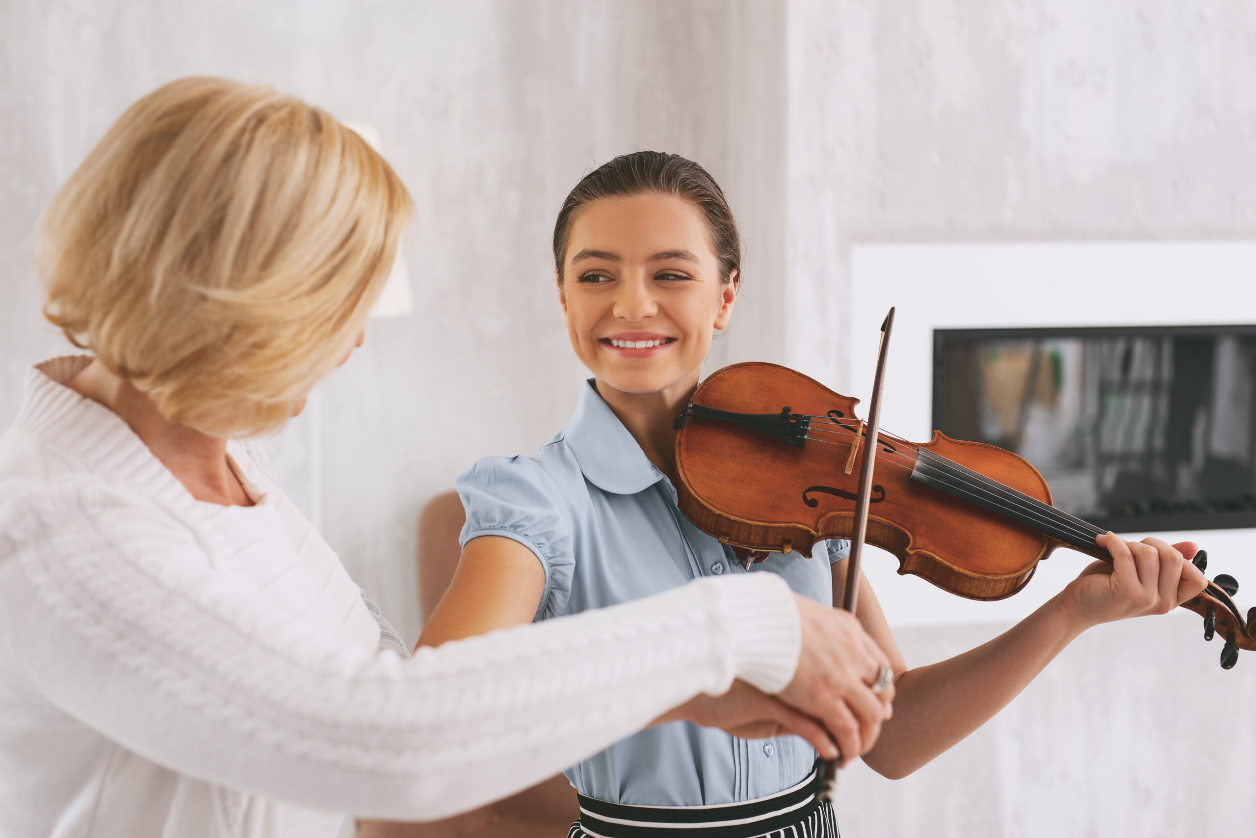 Joyful young woman keeping smile on her face while playing the violin