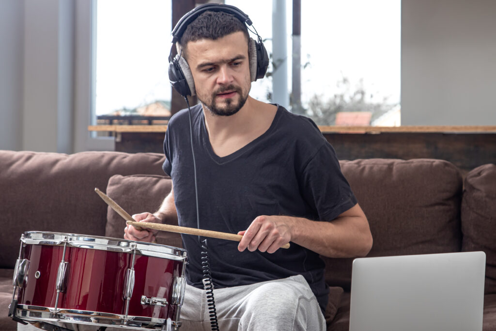 A young man with headphones learns to play the drum using online lessons.