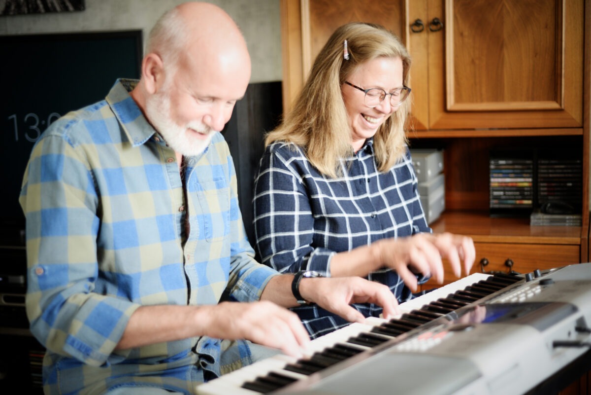 Benefits of piano lessons: Cheerful senior couple playing piano four hands at home