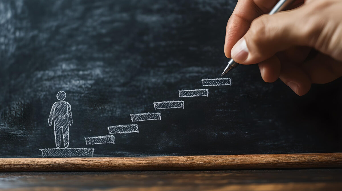 A hand draws steps on a blackboard, symbolizing the journey of personal growth and development.